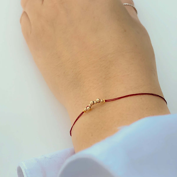 Close-up of hand wearing delicate red thread bracelet with gold beads detail at center.