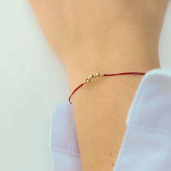 Close-up of hand wearing delicate red thread bracelet with gold beads detail at center.