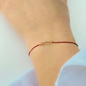 Close-up of hand wearing delicate red thread bracelet with gold beads detail at center.