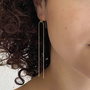 Close-up front view of woman wearing gold earring with two delicate chains that hang down.