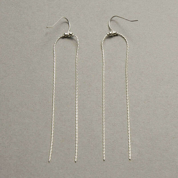 Pair of silver earrings with two delicate chains that hang down with earwire to either side shown on gray background.