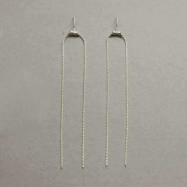Pair of silver earrings with two delicate chains that hang down on a gray background.