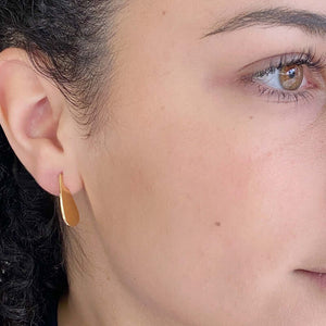 Close-up side view of woman wearing small flat teardrop earrings.