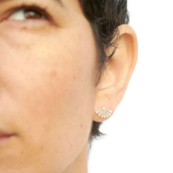 Close-up front view of woman wearing fan-shaped gold earrings with lace pattern.