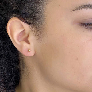 Close-up side view of woman wearing small gold earrings with two gold stacked beads on a post.