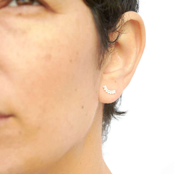 Close-up front view of woman wearing gold earrings, arc-shaped with little triangular beads.