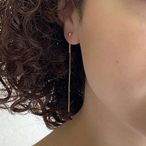 Close-up front view of woman wearing gold dangle earrings, chain with thin bar on ear post.