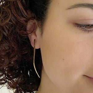Close-up front view of woman wearing gold spike earrings, flat spike with a slight curve at tip.