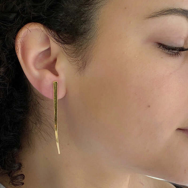 Close-up side view of woman wearing gold spike earrings, flat spike with a slight curve at tip.