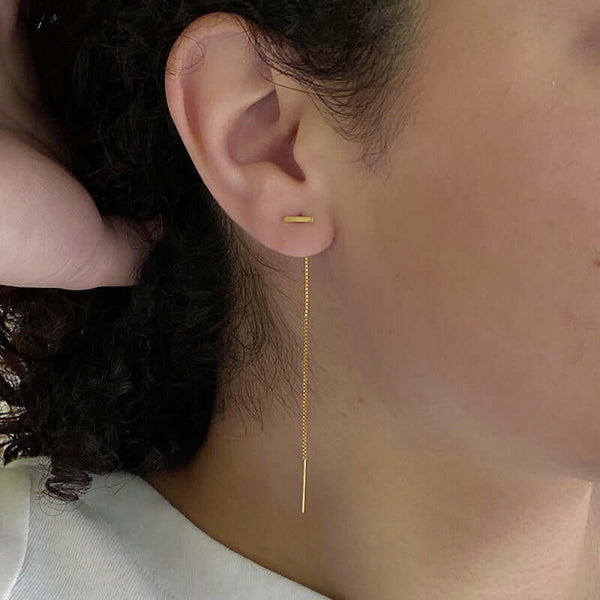 Close up side view of woman wearing gold threader earrings, small bar with fine gold chain ending in bar.