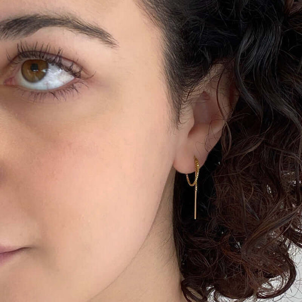 Close up front view of woman wearing gold threader earrings, small bar with thin chain ending in bar, looped twice in ear.