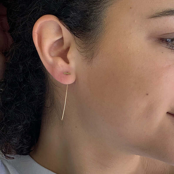 Close-up side view of woman wearing gold bar threader earrings with wire bar extending down.