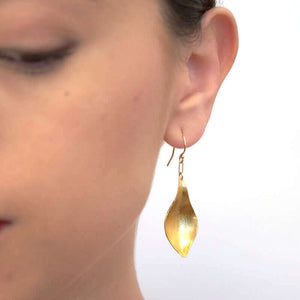 Close-up front view of woman wearing gold earrings, with curved simple leaf design.
