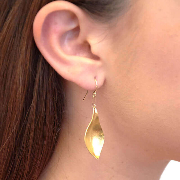 Close-up side view of woman wearing gold earrings, with curved simple leaf design.