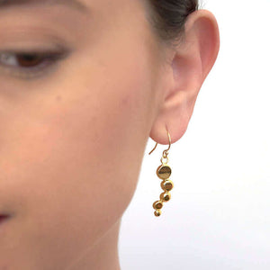 Close-up front view of woman wearing gold earrings with flattened beads of descending size.