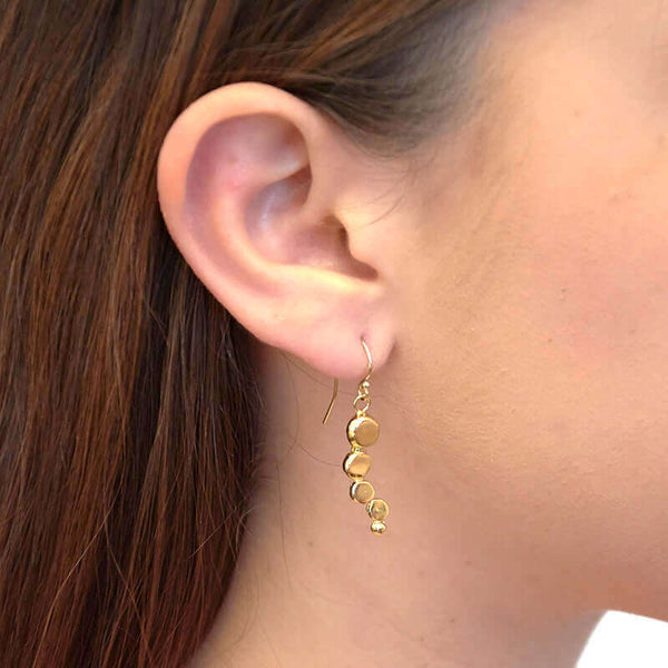 Close-up side view of woman wearing gold earrings with flattened beads of descending size.