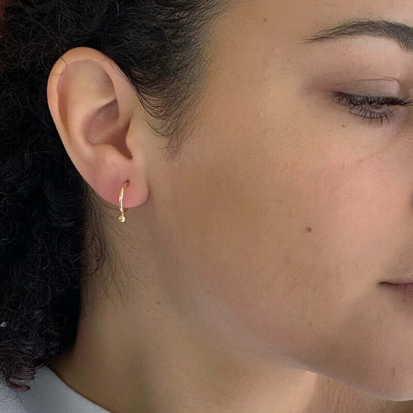 Closeu-p side view of woman wearing small gold hoop earring with small dot bead on bottom.