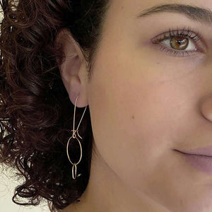 Front view of woman wearing gold earrings with large and small interlocked circles on long earwire.