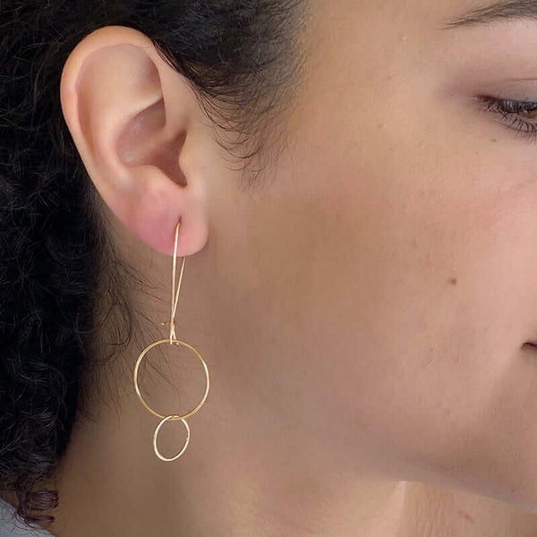 Side view of woman wearing gold earrings with large and small interlocked circles on long earwire.