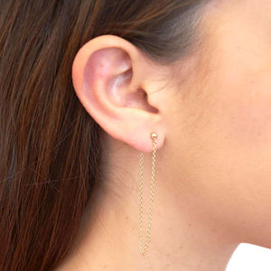 Side view of woman wearing gold earrings, long loop of delicate chain on a post.