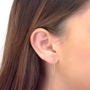 Side view of woman wearing gold earrings, short loop of delicate chain on a post.