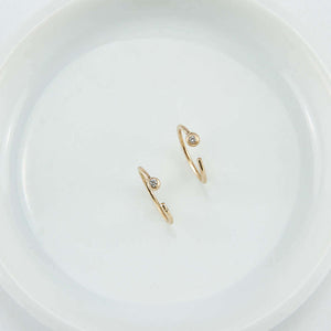 Pair of small gold hoop earring, tiny ball detail in front with inset diamond, facing up.