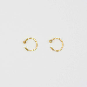 Pair of small gold hoop earring with a tiny ball detail in front, facing sideways.