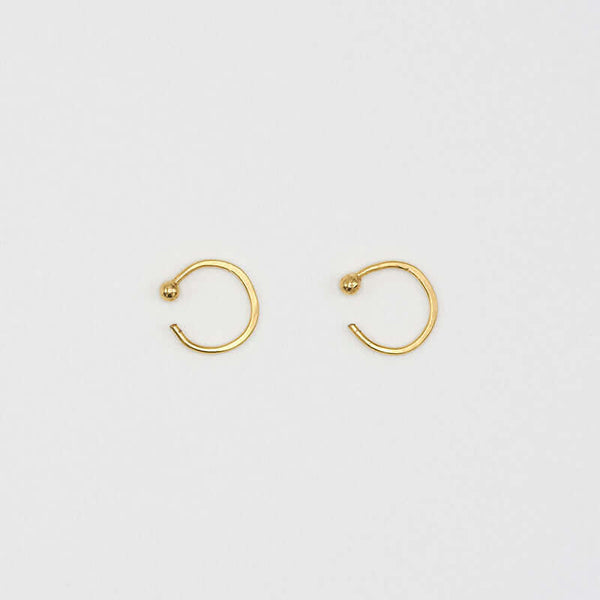 Pair of small gold hoop earring with a tiny ball detail in front, facing sideways.
