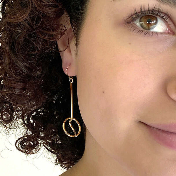 Close up front view of woman wearing gold earrings, bent round wire with a straight drop to circle detail.