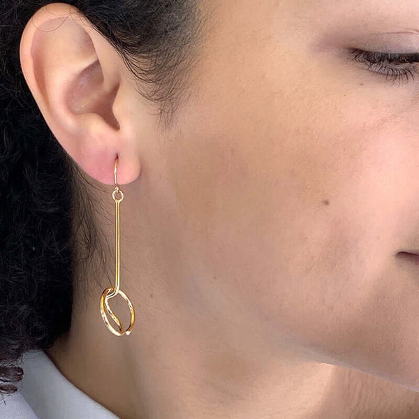 Close up side view of woman wearing gold earrings, bent round wire with a straight drop to circle detail.