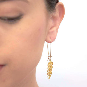 Close up front view of woman wearing gold fern leaf shaped earrings on long earwire.
