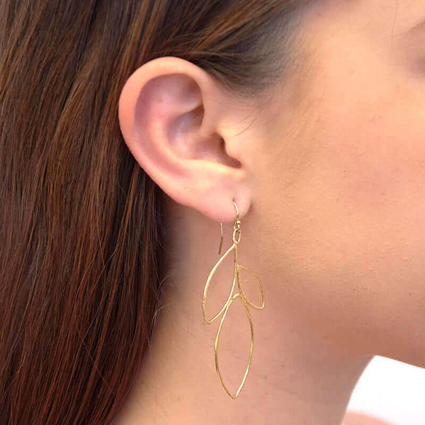 Close-up side view of woman wearing gold earrings shaped like outline of group of leaves.