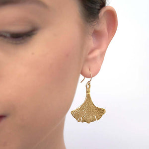 Close up front view of woman wearing gold earrings shaped like ginko leaves.