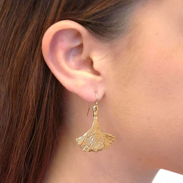 Close-up side view of woman wearing gold earrings shaped like ginko leaves.