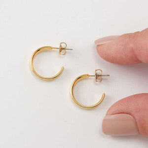 Pair of gold open hoop earrings on posts, with fingers for scale.