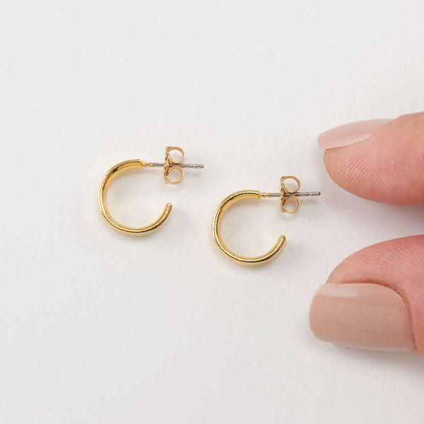 Pair of small gold open hoop earrings on posts, with fingers for scale.