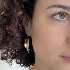Close up front view of woman wearing gold earrings, with curved diamond design.