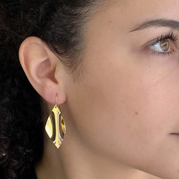 Close up side view of woman wearing gold earrings, with curved diamond design.