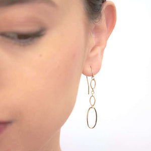 Close up front view of woman wearing gold oval chain earrings, with large oval link at end.