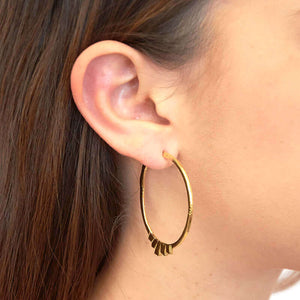 Close up side view of woman wearing pair of silver geometric native motif hoop earrings.