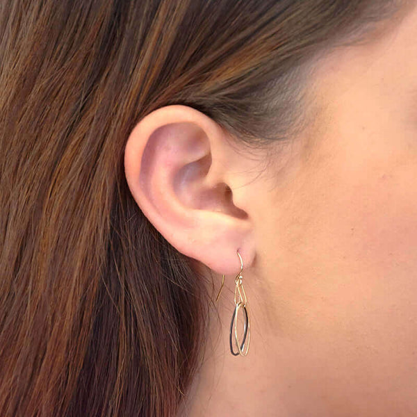 Close up side view of woman wearing pair of earrings with silver, black and gold colored oval links on gold earwire.