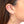 Close up side view of woman wearing pair of silver geometric rhombus shaped hoop earrings.