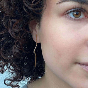 Close-up front view of woman wearing pair of gold wire earrings with geometric zig zag design.
