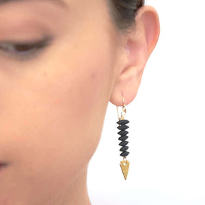 Close up front view of woman wearing pair of gold earrings with black beads and hammered arrowhead detail at end.