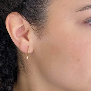 Close up side view of woman wearing pair of small gold wire earrings with gold beads.