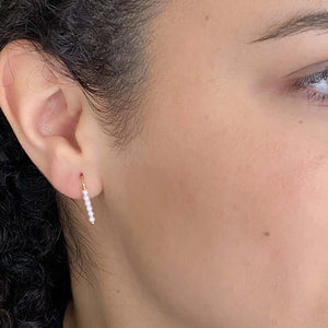 Close up side view of woman wearing pair of small gold wire earrings with pearl beads.