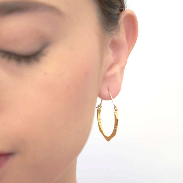 Close up front view of woman wearing pair of cast brushed gold hoop style earrings.