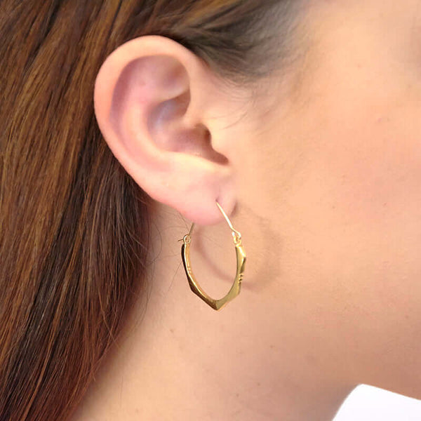 Close up side view of woman wearing pair of cast brushed gold hoop style earrings.