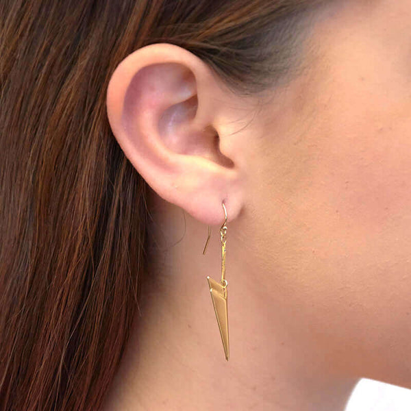 Close up side view of woman wearing pair of gold chevron shaped earrings on earwire.