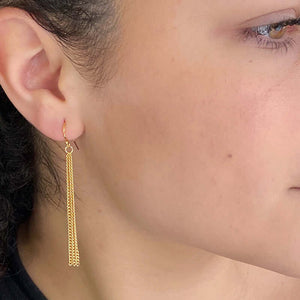 Close up side view of woman wearing pair of of gold chain tassel earrings, on earwire.